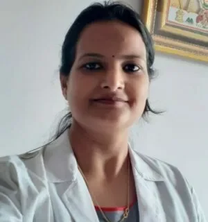 Dr. Anjana A woman in a white lab coat stands in front of a painting at Jain Surgical Hospital in Kota, the best hospital in Kota.